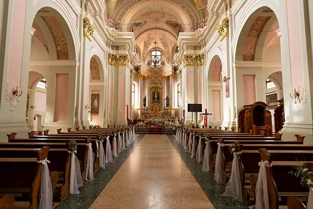 A large church with a long aisle of pews and a large altar The pews are empty and the altar is covered in flowers - Best Travel Agents in NJ - JJ Travel Associates Inside of a beautiful cathedral