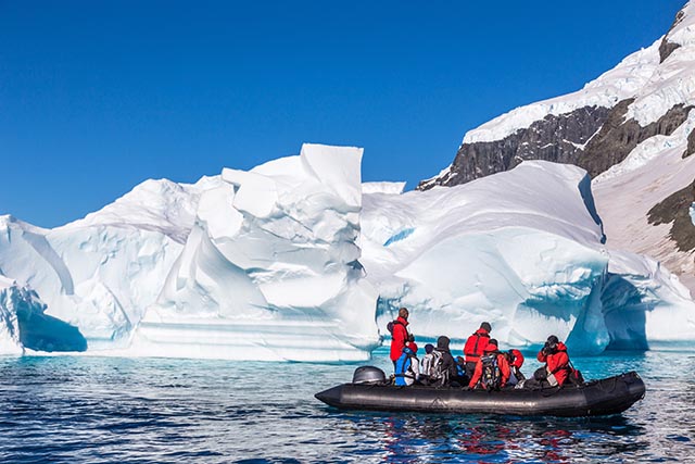 People on an expedition cruise, riding in a zodiak near icebergs.